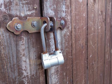 Eski, paslı, beyaz bir metal kilidin, eski kahverengi ahşap bir kapının girişini kapatması.