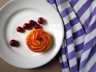 Kirazlar ve çörekler beyaz bir tabakta, masanın üzerinde çizgili bir bezle.