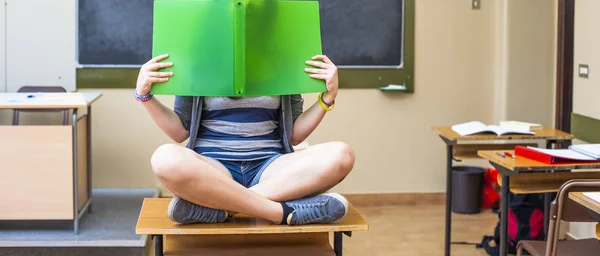 Student cover her face with a book in classroom