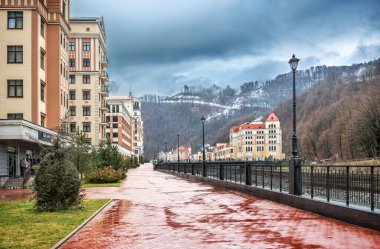 Yağmurlu bir günde Soçi 'de Rosa Khutor' daki otellerin, dükkanların, Mzymtu nehrinin ve dağların karlı zirvelerinin manzarası..