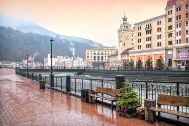 Yağmurlu bir günde Rosa Khutor, Soçi 'deki dükkanların, kafelerin, belediye kulesinin, nehrin ve dağların karlı zirvelerinin manzarası..