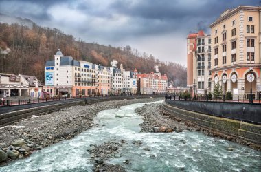 Yağmurlu bir günde Soçi 'deki Rosa Khutor' daki dükkanların, otellerin, kafelerin, Mzymtu Nehri 'nin ve dağların karlı zirvelerinin manzarası..