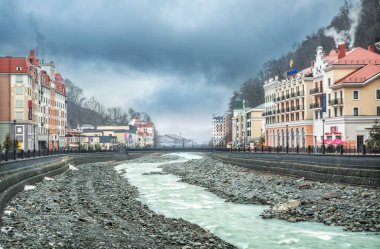 Yağmurlu bir günde Soçi 'de Rosa Khutor' daki dükkanların, kafelerin, Mzymta Nehri 'nin ve dağların karlı zirvelerinin manzarası.