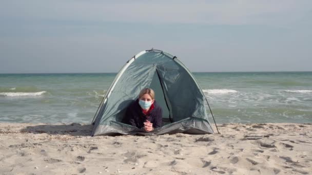 護身用のマスクをした若い女性が海岸にテントを張っている 隔離された場所 コロナウイルスの流行から逃れる 観光シーズンの失敗 — ストック動画