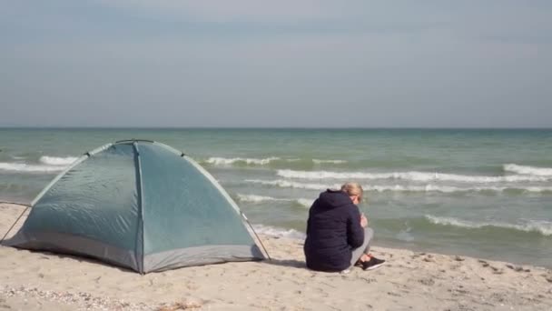 年轻的女游客坐在帐篷附近的海滨 在智能手机上拍照 — 图库视频影像