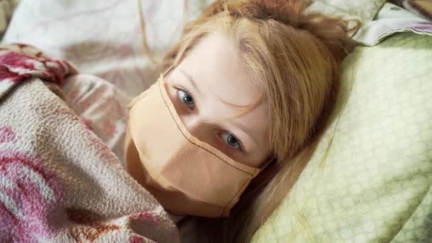 小女孩病了 躺在床上 戴着医疗面罩 裹着一条毯子 小女孩有一双流露的眼睛 躺在被子下面的床上 — 图库视频影像