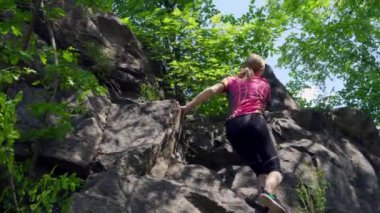 Spor elbiseli genç bir kadın kayalık bir dağa tırmanır. Adımlarını düşünüyor..