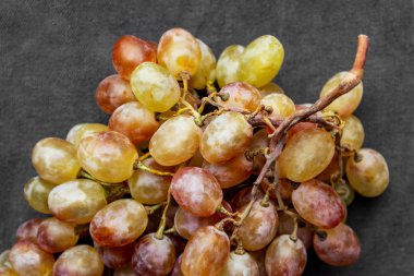 Gri kumaş arka planında izole edilmiş bir demet üzüm, bir demet olgun yeşil ve yapraksız sarı üzüm.