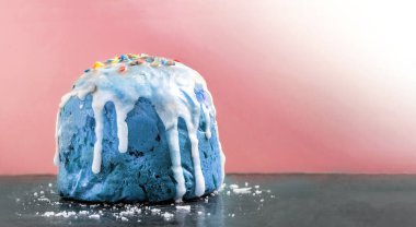 Paskalya pastası klasik maviye boyanmış beyaz akıcı krema ve siyah bir yüzeye yakın duran pembe arka planda buz kırıntıları olan renkli konfeti.