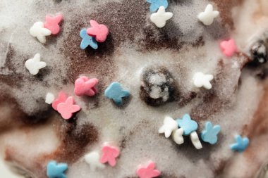 Şeker renkli konfeti beyaz kremalı kekin üzerinde uzanıyor. Kek yüzeyine şeker kreması dokusu yakın plan, pembe, mavi ve beyaz şeker.