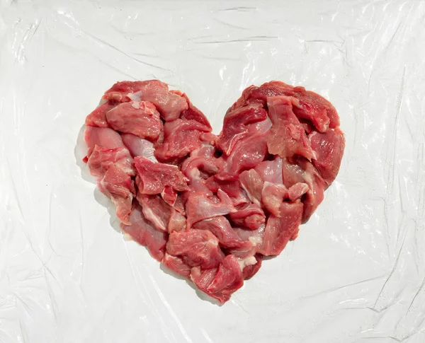 Carne fresca en forma de corazón sobre fondo blanco con película de alimentos, chuleta para chuletas — Foto de Stock