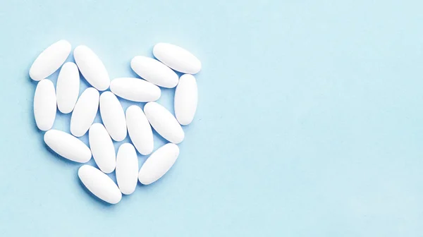 Srdce ve tvaru lékařské bílé oválné pilulky izolované na modrém pozadí. — Stock fotografie