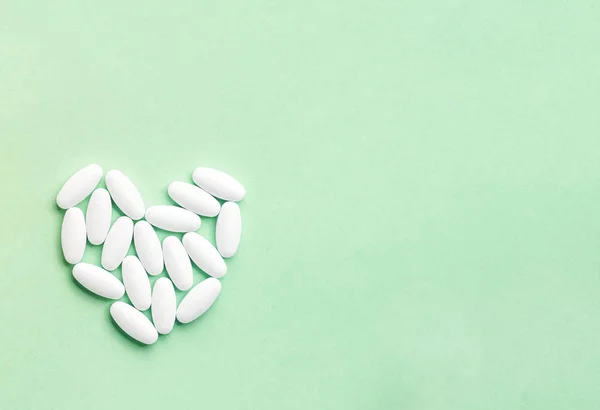 Léky bílé oválné tablety ve formě srdce izolované na zeleném pozadí, koncepce léčby a zdravotní péče — Stock fotografie