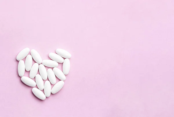 Bílé srdce z tablet a pilulky izolované na růžovém pozadí se slunečním světlem. — Stock fotografie