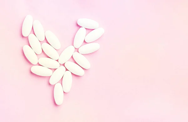 Bílé srdce z tablet a pilulky izolované na růžovém pozadí se slunečním světlem. — Stock fotografie