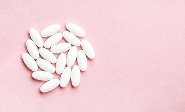 Pembe arka planda güneş ışığıyla izole edilmiş tablet ve haplardan oluşan beyaz daire..
