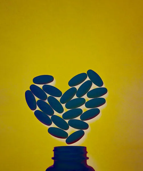 Классические синие таблетки в форме сердца с бутылкой, нарисованной на желтом фоне. Витамины для здоровья, безопасные таблетки. Копирование текста — стоковое фото