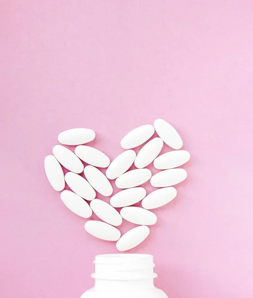 Bílé pilulky ve tvaru srdce s lahví na růžovém pozadí. Kopírovat prostor pro text — Stock fotografie