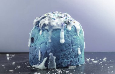 Klasik maviyle boyanmış pasta, beyaz akıcı krema ve renkli konfeti, siyah bir yüzeye yakın, buz kırıntıları ile birlikte.