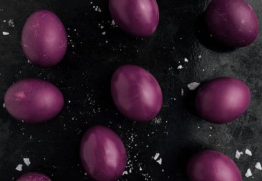 Mor monokrom tarzında boyanmış Paskalya yumurtaları buzlu kırıntılarla kaplanmış siyah bir yüzeye yakın dururlar. Lekeli yumurtalar, çizikler, çizikler. El yapımı boyanmış yumurta. Düz yatıyordu