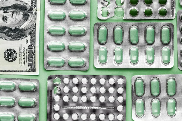 white and green pills in blister with money on a green background, medicine flat lay