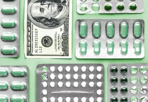 white and green pills in blister with money on a green background, medicine flat lay