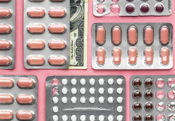 White and pink pills in blister with money dollar hidden under the pills on a pink background, medicine flat lay — Stock Photo, Image