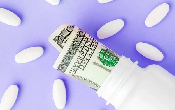 Roll geld Facturen in witte pil fles met witte pillen. De hoge kosten van de gezondheidszorg. Pillen en Amerikaanse valuta in Pil flessen — Stockfoto