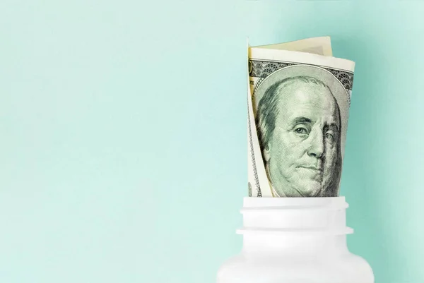 Roll of money Bills in white pill bottle on Aqua Menthe background with copy space. medicine flat lay — Stock Photo, Image