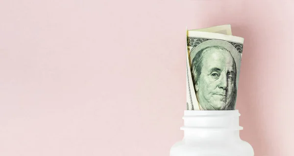 Roll of money Bills in white pill bottle on pink background with copy space. medicine flat lay — Stock Photo, Image