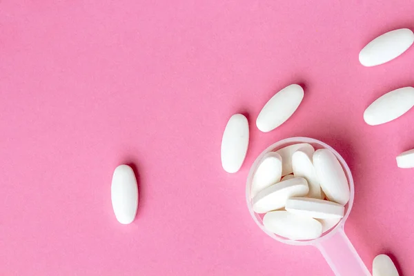 Bílé pilulky v lžičce na léky na růžovém pozadí, zblízka — Stock fotografie