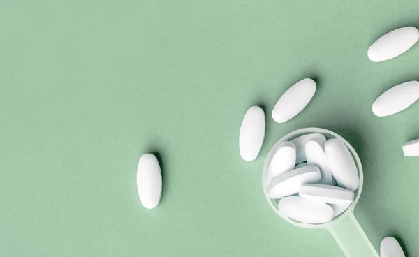 White pills in dosage spoon for drugs on a Aqua Menthe background, close-up — Stock fotografie