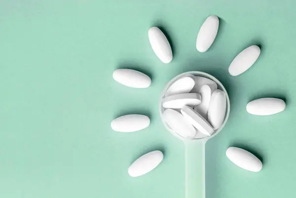 White pills in dosage spoon for drugs in the shape of a flower on a Aqua Menthe background, close-up — Stock fotografie