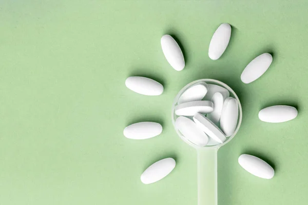Bílé pilulky v lžíci na léky ve tvaru květiny na zeleném pozadí, detailní záběr — Stock fotografie