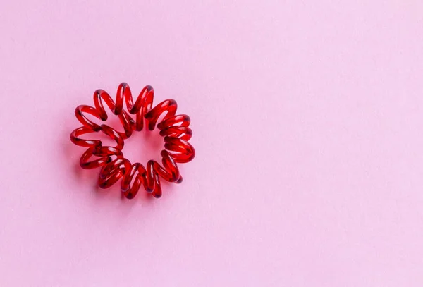 Faixa de borracha espiral vermelha torcida. laço de cabelo elástico no fundo rosa close-up, espaço de cópia — Fotografia de Stock