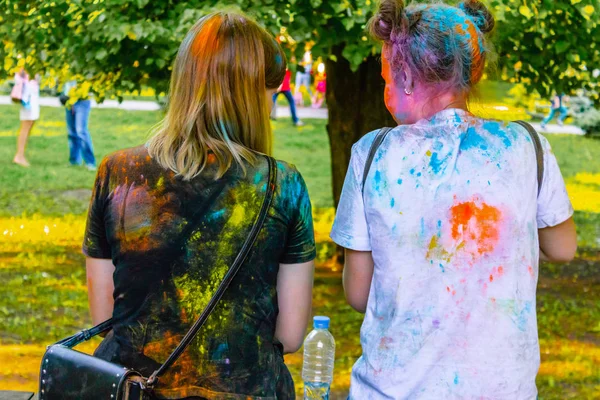 Ufa, Russland - 5. Juli 2019: Zwei Teenager-Mädchen in weißen und schwarzen T-Shirts, die mit Holi-Puderfarbe befleckt sind, Blick von hinten, vor der Kulisse eines grünen Rasens im Sommer lizenzfreie Stockfotos