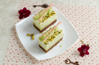 Çağdaş kirazlı ve şam fıstıklı kremalı kekler beyaz tabakta beyaz çiçeklerle süslenmiş.