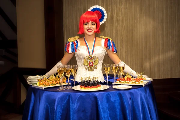 Moscou, Rússia - 18 de setembro de 2016: Buffet de senhora encantadora, que se veste é estilizado cores nacionais russas e o brasão de armas, com uma mesa na forma de saias recebe os hóspedes com alimentos e bebidas . — Fotografia de Stock
