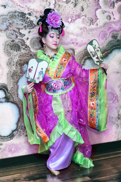 Portret van een jonge Chinese vrouw in klederdracht met fans, volledige lengte tegen marmeren muur achtergrond. — Stockfoto