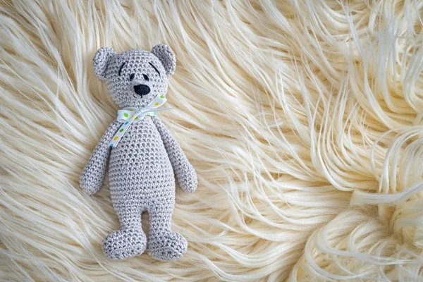 Cute handmade crochet amigurumi teddy bear doll laying on the white fur with copy space