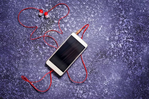 Мобильный телефон с наушниками для прослушивания музыки. Красный кабель в форме бабочки или сердца. Скопируйте место для вашей надписи. Ремонтный валет . — стоковое фото