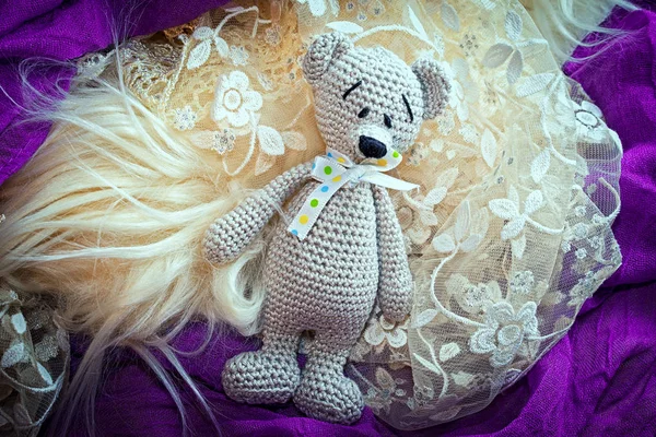 Knitted amigurumi doll bear laying on a fur and lace — Stock Photo, Image