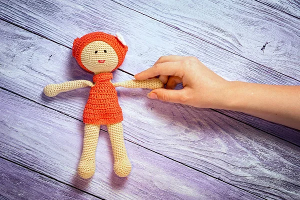 Crocheted doll girl and this girl 's hand on the wooden background with free place for your inscription — стоковое фото