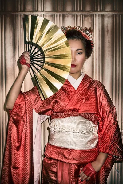 Asyalı kadın yüzünün yarısını kapsayan bir kağıt fan tutan geleneksel kırmızı Kimono içinde. — Stok fotoğraf