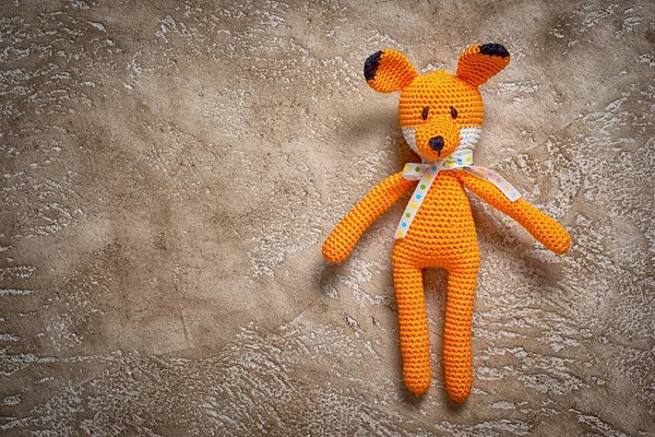 crocheted amigurumi fox toy on a neutral brown cement background with copy space