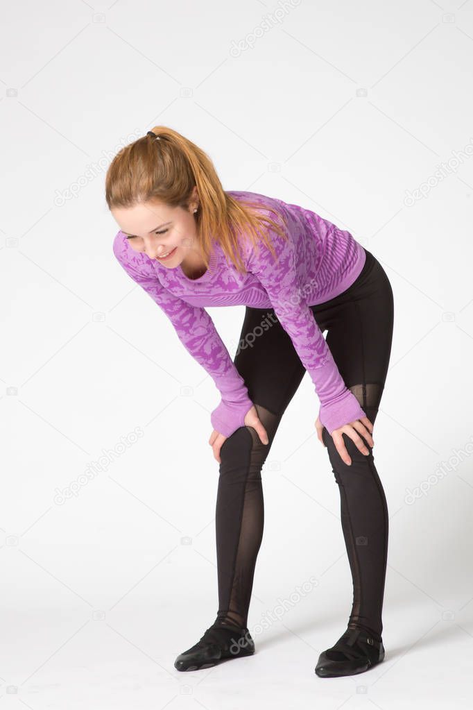 Girl in sportswear relaxing after a workout, standing hunched over and leaning her hands on the legs