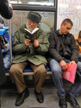 Moskova, Rusya - 03 Aralık 2016: röportaj Moskova metrosu görüntüleri. Yolcular trende seyahat. Yaşlı adam iki gözlük bir tren oturan bir kitap okuma.
