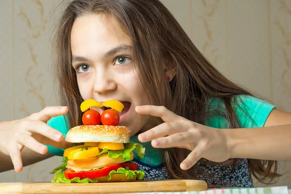 Menina de 11 anos salta em um hambúrguer, o conceito de fome e hábitos alimentares pouco saudáveis . — Fotografia de Stock