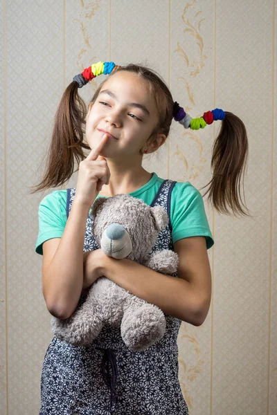 11-jähriges Mädchen mit Teddybär blickt nachdenklich mit dem Finger zum Mund auf. — Stockfoto