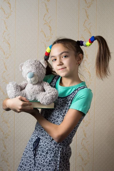 Glückliches 11-jähriges Mädchen mit lustigem Schwanz hält ein Buch und einen Teddybär in der Hand — Stockfoto